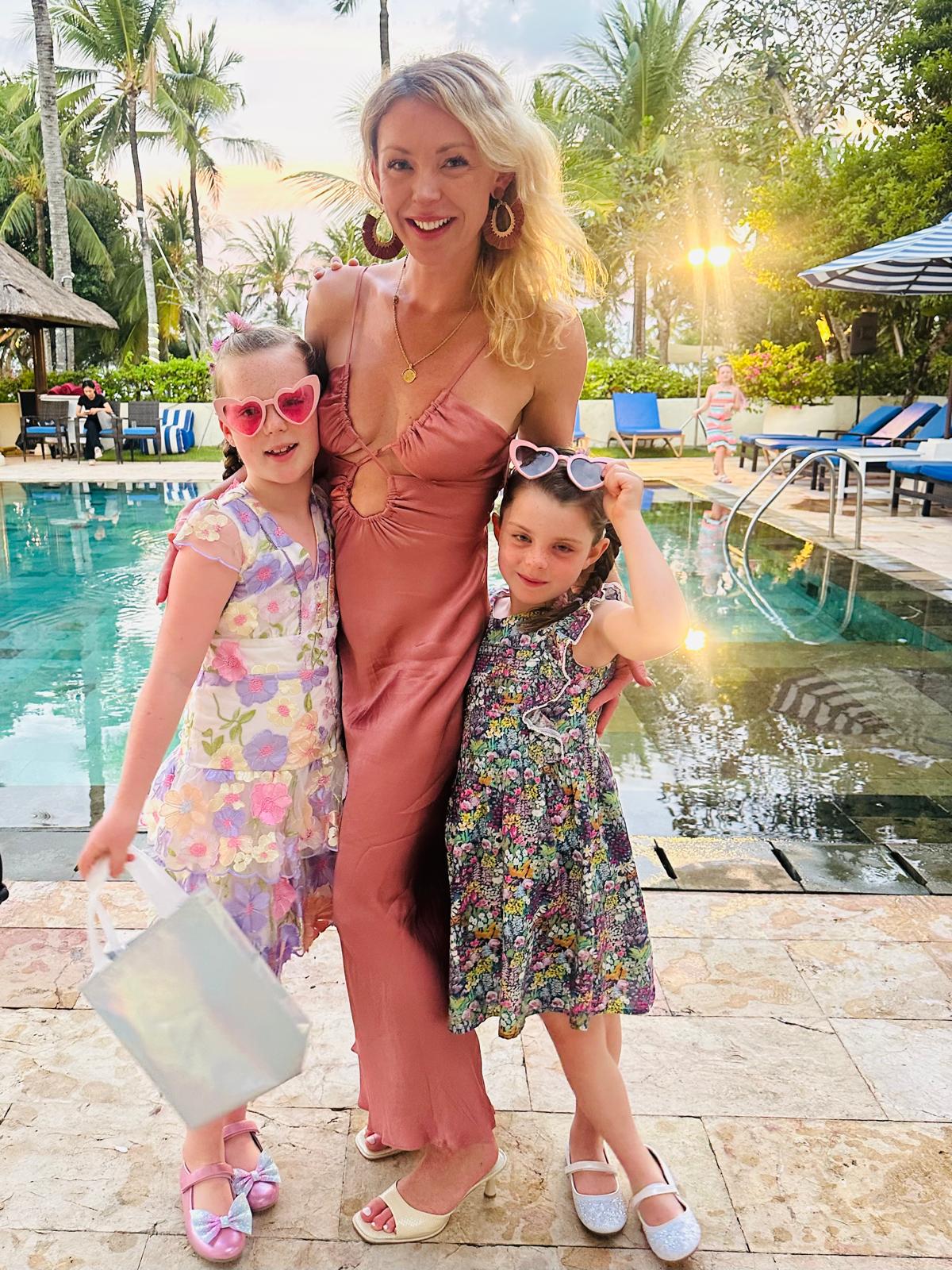 Woman in a pink dress with two children by a poolside